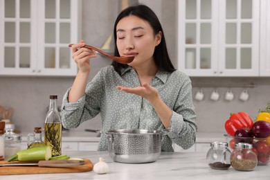 Beautiful woman tasting food after cooking in kitchen