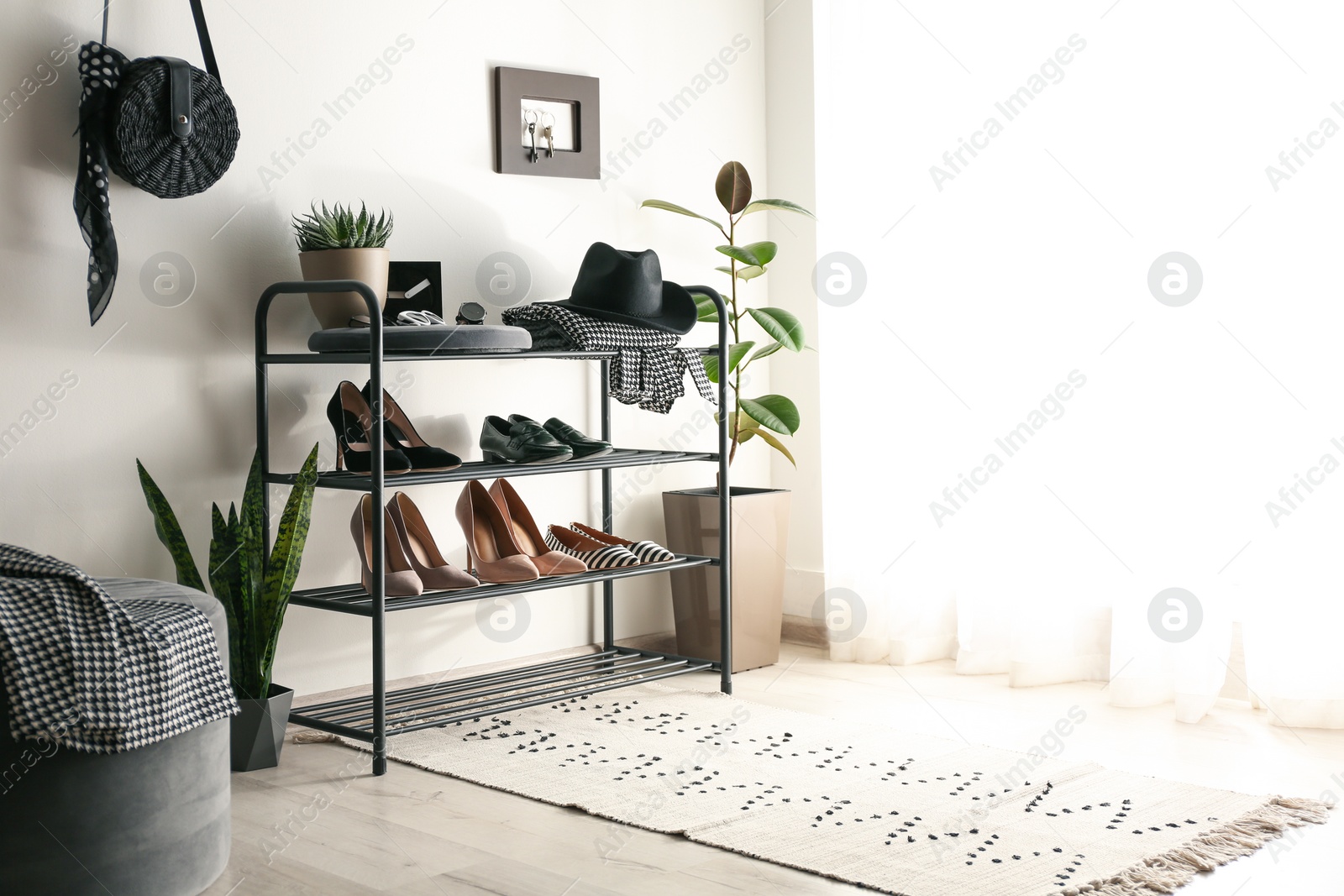 Photo of Black shelving unit with shoes and different accessories near white wall in hall