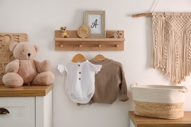 Photo of Wooden shelf with baby clothes, toys and furniture in room. Interior design
