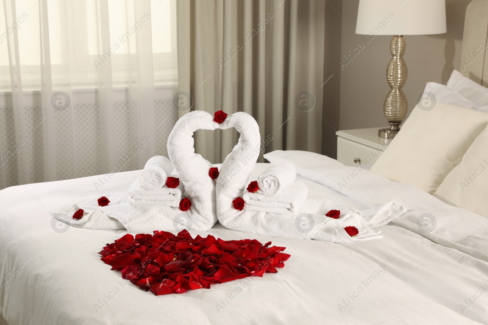 Photo of Beautiful composition on bed. Swans made of towels and rose petals arranged in heart shape