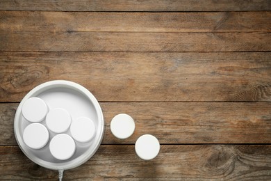 Modern yogurt maker with jars on wooden table, flat lay. Space for text