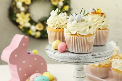 Photo of Tasty Easter cupcakes with vanilla cream and festive decor on table