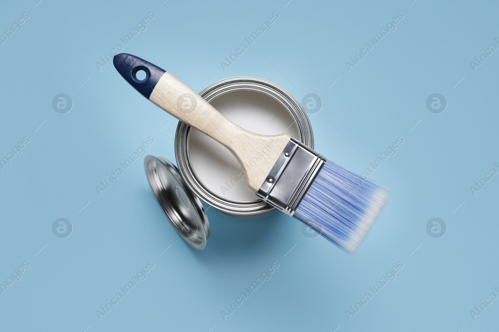 Photo of Can with white paint and brush on light blue background, top view