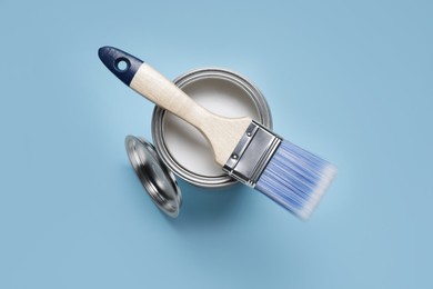 Photo of Can with white paint and brush on light blue background, top view