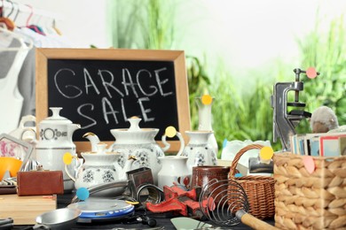 Photo of Blackboard with sign Garage Sale and many different stuff on black wooden table indoors