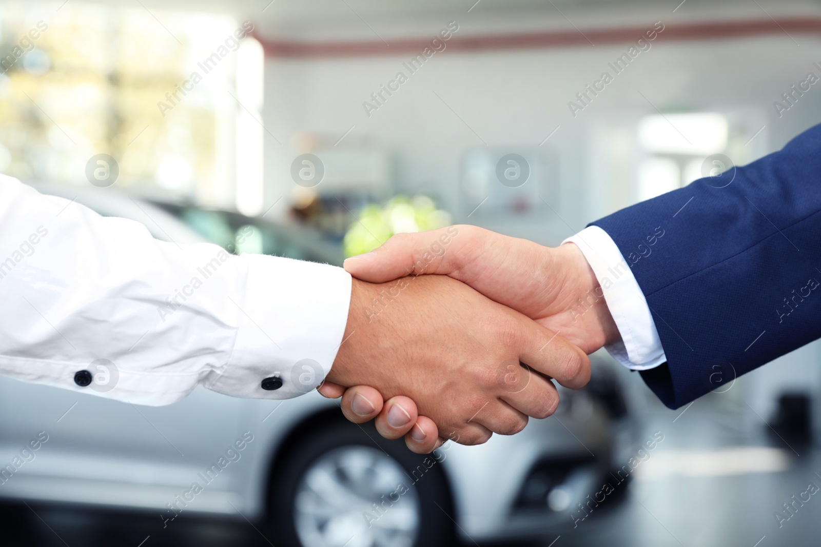 Photo of Young car salesman shaking hands with client in dealership, closeup