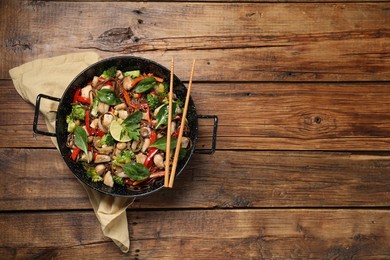 Photo of Stir-fry. Tasty noodles with meat in wok and chopsticks on wooden table, top view. Space for text