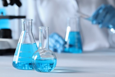 Photo of Closeup view of scientist pouring light blue liquid from test tube into flask and laboratory glassware on table, selective focus