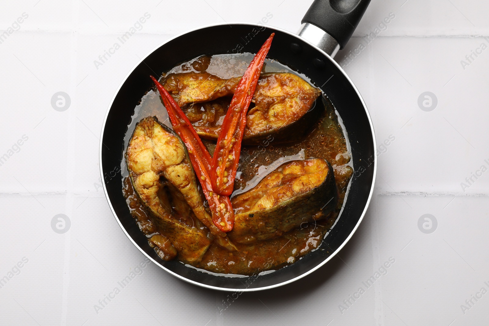 Photo of Tasty fish curry in frying pan on white tiled table, top view. Indian cuisine