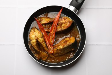 Photo of Tasty fish curry in frying pan on white tiled table, top view. Indian cuisine