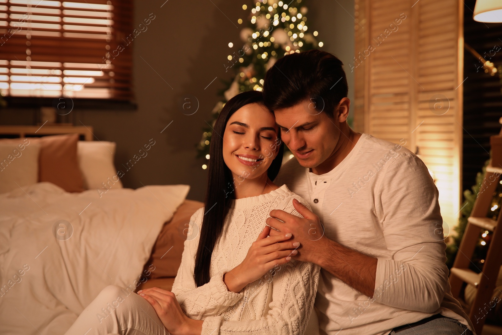 Photo of Happy couple sitting in festively decorated bedroom. Christmas celebration