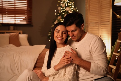 Happy couple sitting in festively decorated bedroom. Christmas celebration