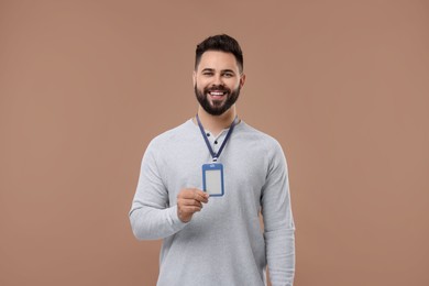 Happy young man with blank badge on beige background