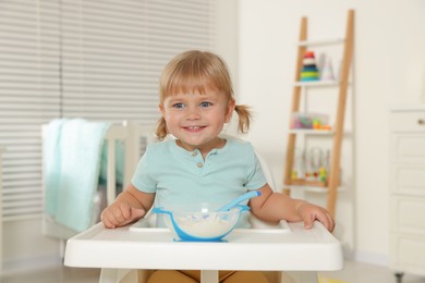 Cute little child eating tasty yogurt with spoon at home