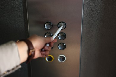 Photo of Woman using pen to choose floor in elevator, closeup. Protective measure