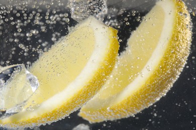 Photo of Juicy lemon slices and ice cubes in soda water against black background, closeup