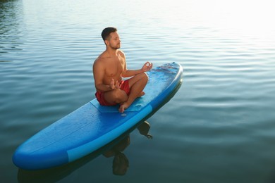 Photo of Man meditating on light blue SUP board on river