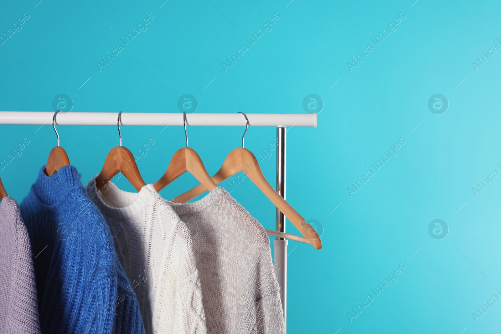 Photo of Collection of warm sweaters hanging on rack against color background. Space for text