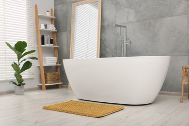 Stylish bathroom interior with soft yellow bath mat and tub