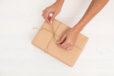 Photo of Woman decorating parcel with twine on wooden background