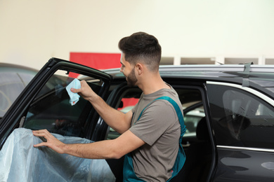 Photo of Worker washing tinted car window in workshop