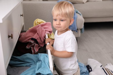 Photo of Cute little boy playing with clothes in dresser's drawer at home