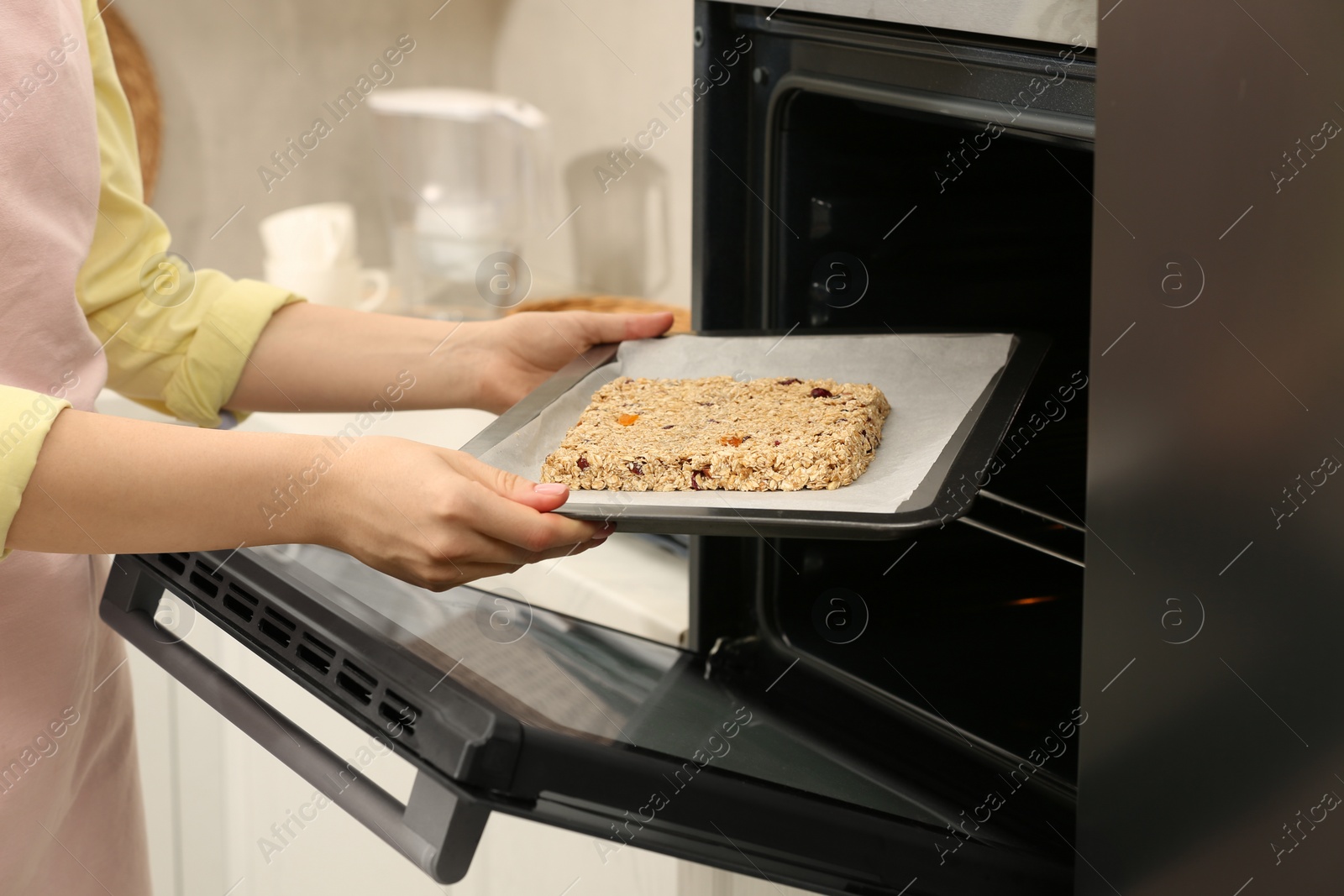 Photo of Making granola. Woman putting baking tray into oven in kitchen, closeup