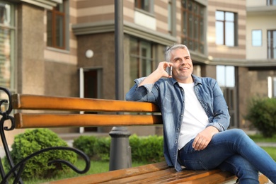 Handsome mature man talking on phone in city. Space for text