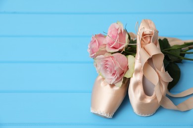 Beautiful beige ballet shoes with cute ribbons and rose flowers on light blue wooden table. Space for text