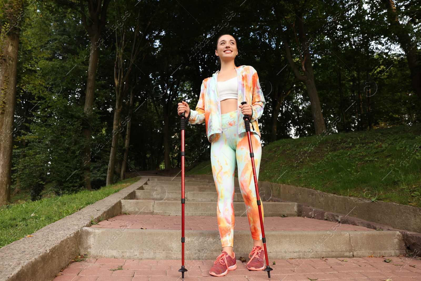 Photo of Young woman practicing Nordic walking with poles on steps outdoors, low angle view