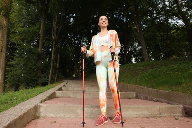 Photo of Young woman practicing Nordic walking with poles on steps outdoors, low angle view