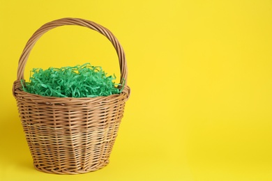 Photo of Easter basket with green paper filler on yellow background, space for text
