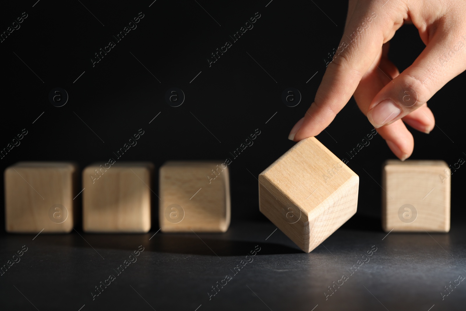 Photo of Woman choosing wooden cube among others at dark table, closeup