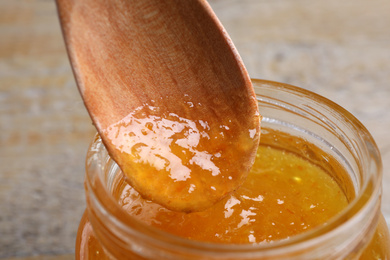 Spoon with apricot jam in jar on table, closeup