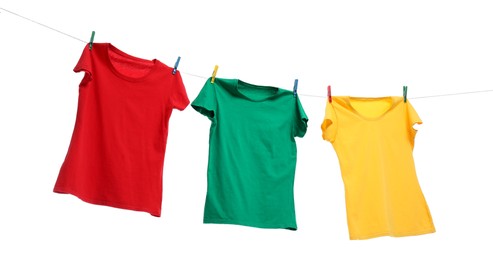Photo of Different bright t-shirts drying on washing line against white background