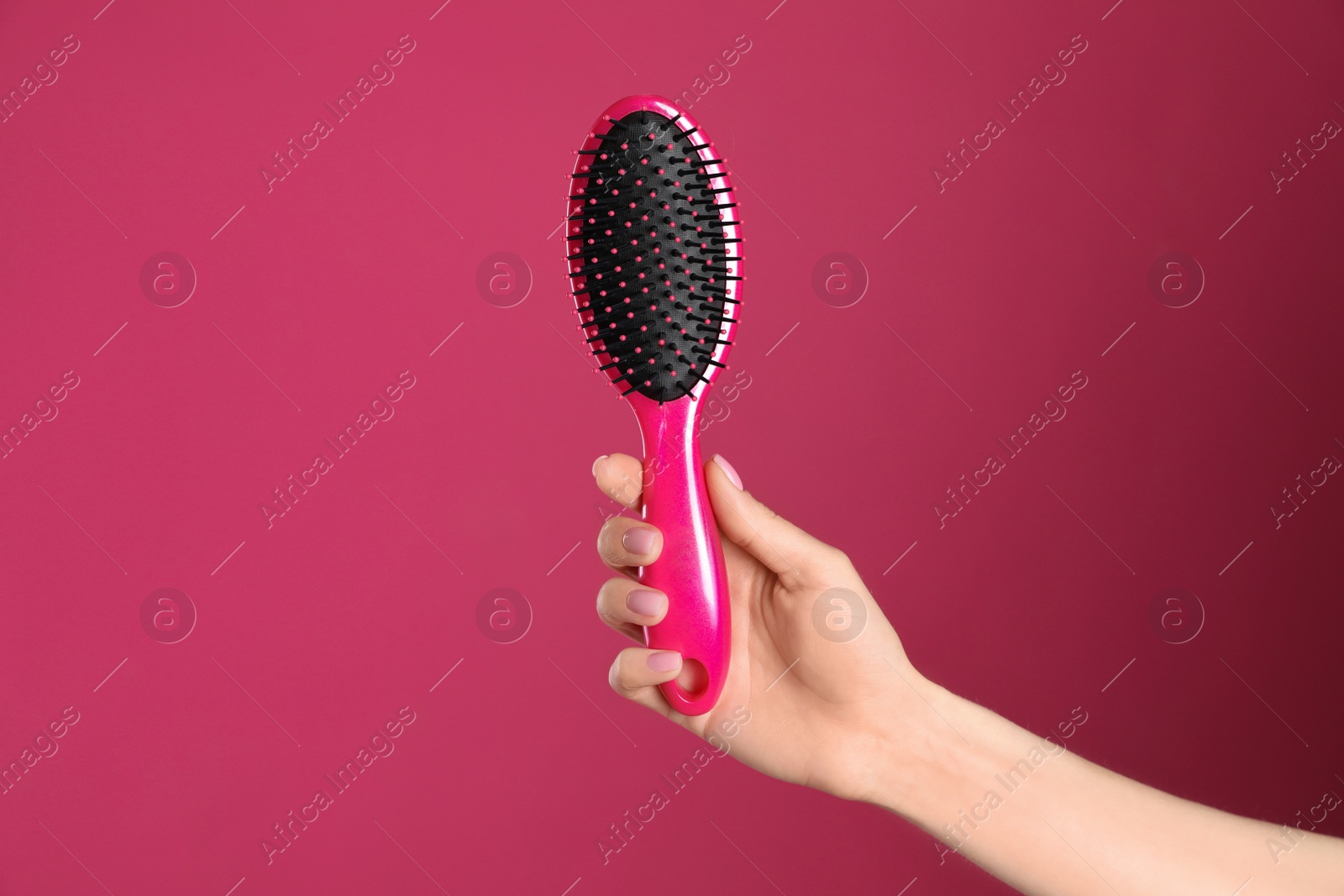 Photo of Woman holding hair brush against crimson background, closeup. Space for text