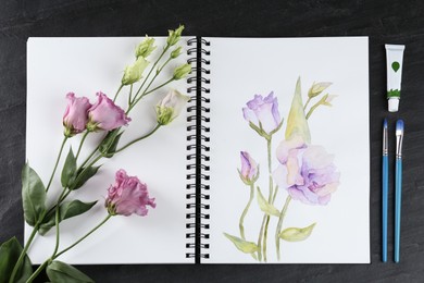 Painting of eustomas in sketchbook, flowers and art supplies on black table, flat lay