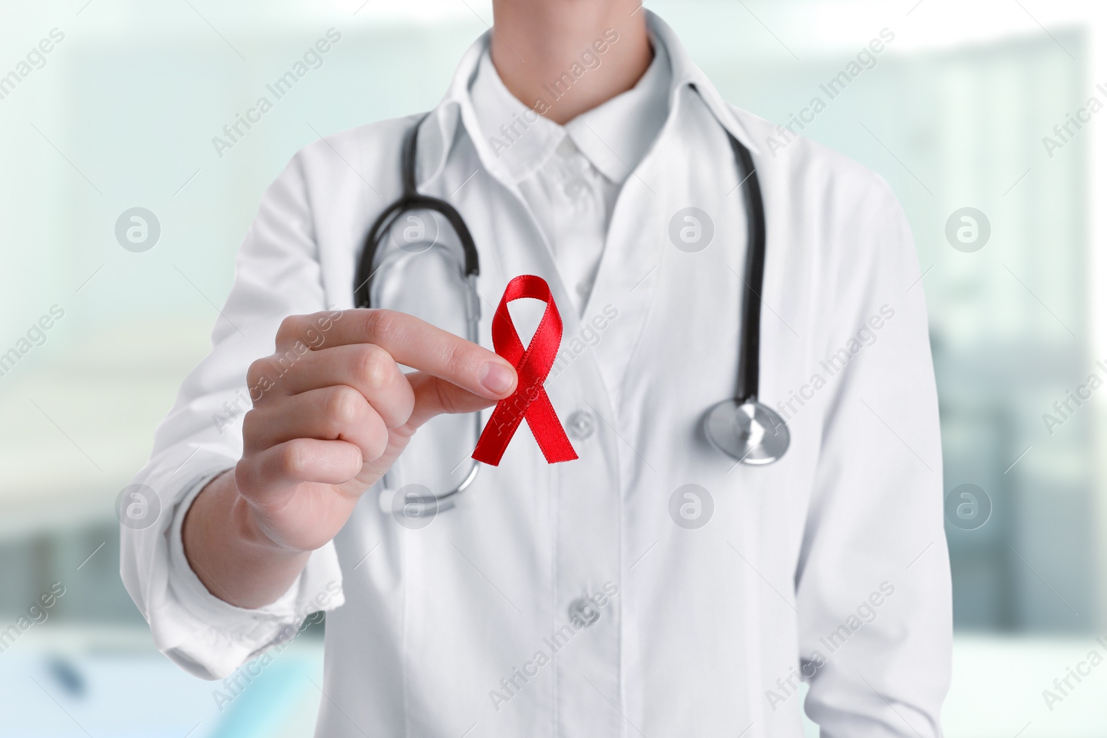 Image of Cancer awareness. Doctor holding red ribbon on blurred background, closeup