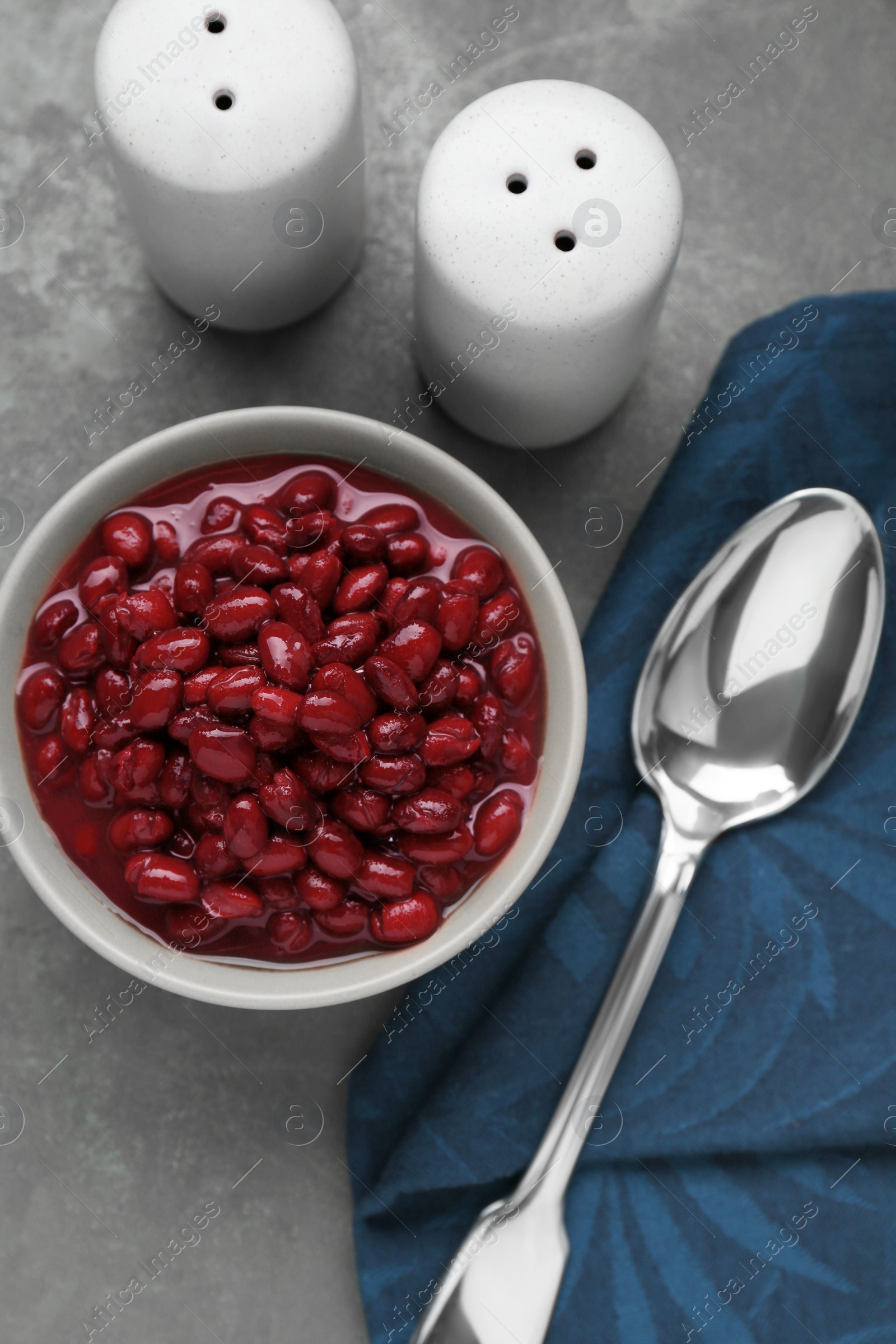 Photo of Bowl of canned kidney beans, spoon and shakers on grey table, flat lay