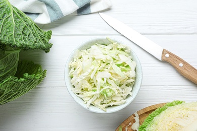 Photo of Cut fresh savoy cabbage in bowl on white wooden table, flat lay