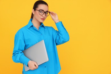 Photo of Young female intern with laptop on yellow background, space for text