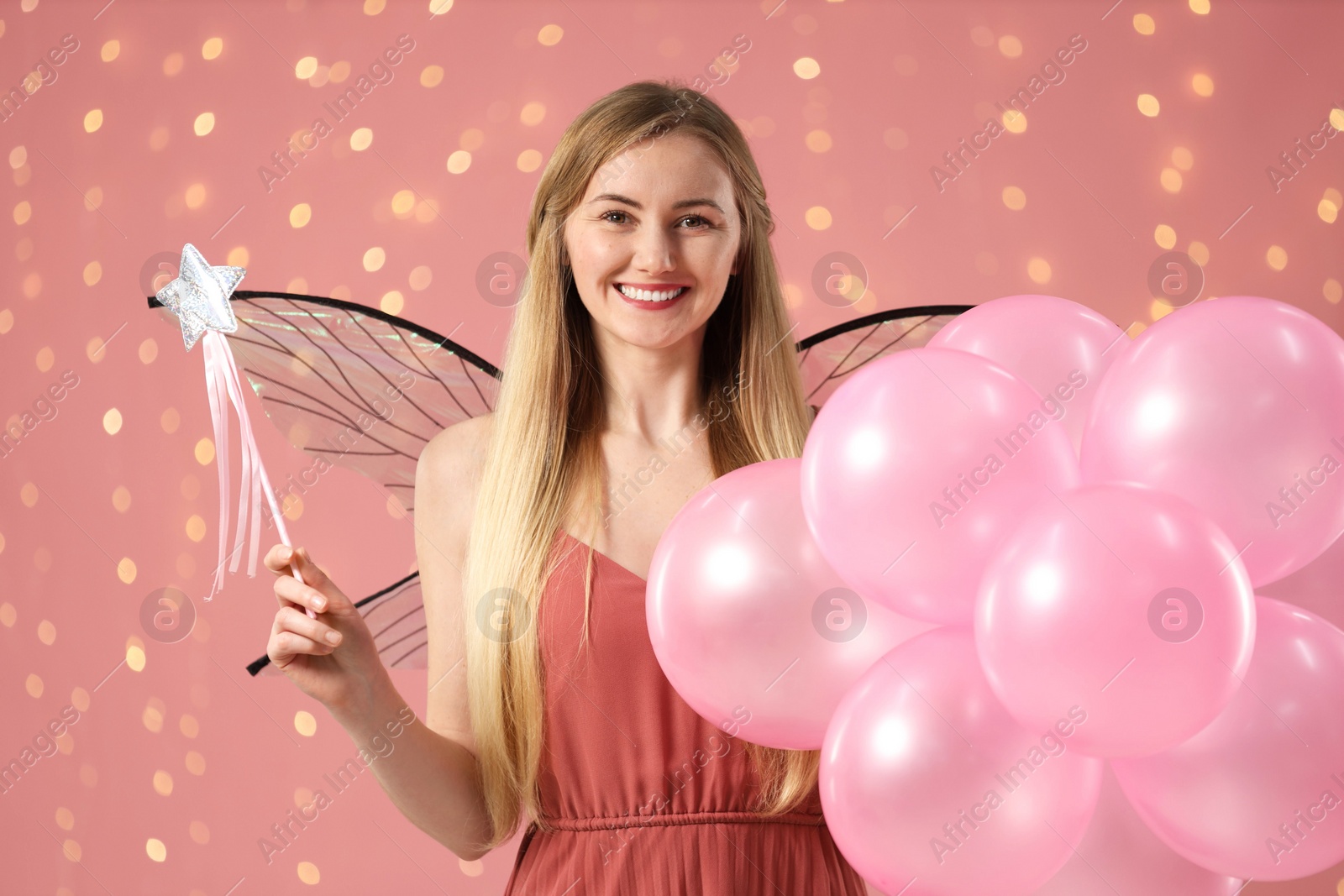 Photo of Beautiful girl in fairy costume with wings, magic wand and balloons on pink background