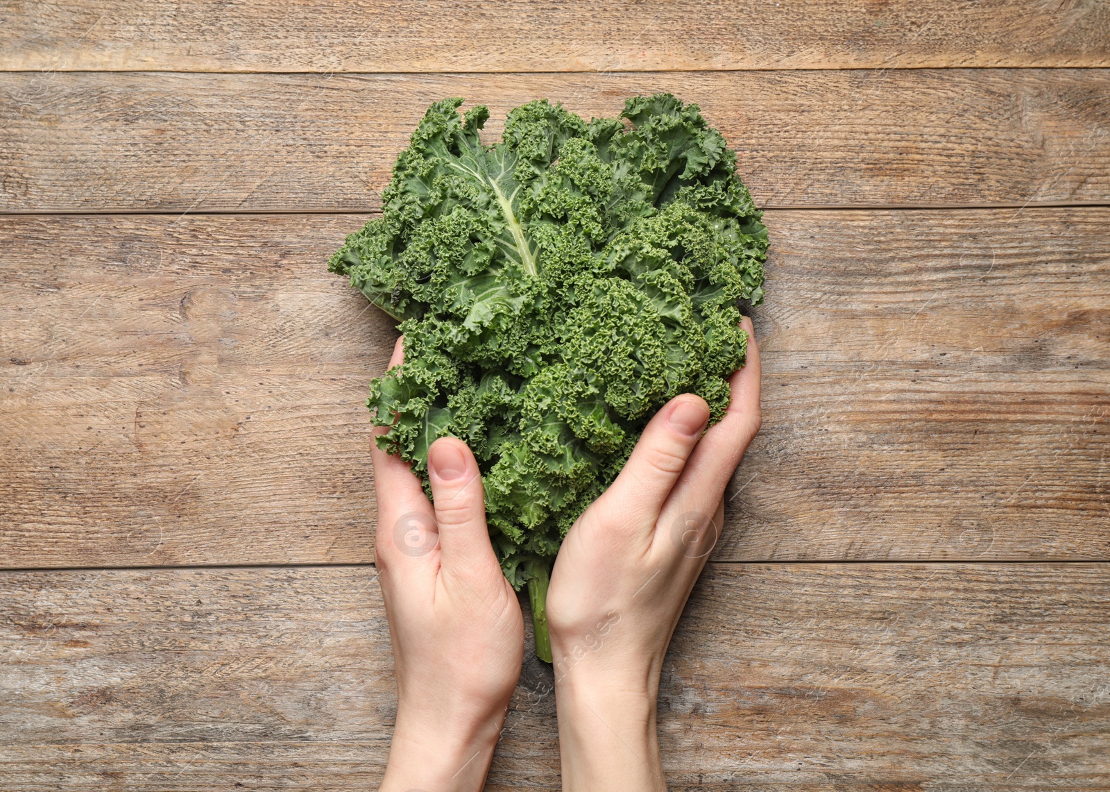 Photo of Woman holding fresh kale leaves on wooden background, top view