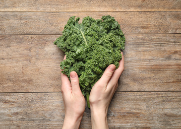 Woman holding fresh kale leaves on wooden background, top view