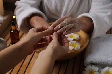 Photo of Woman receiving hand treatment at wooden table in spa, closeup