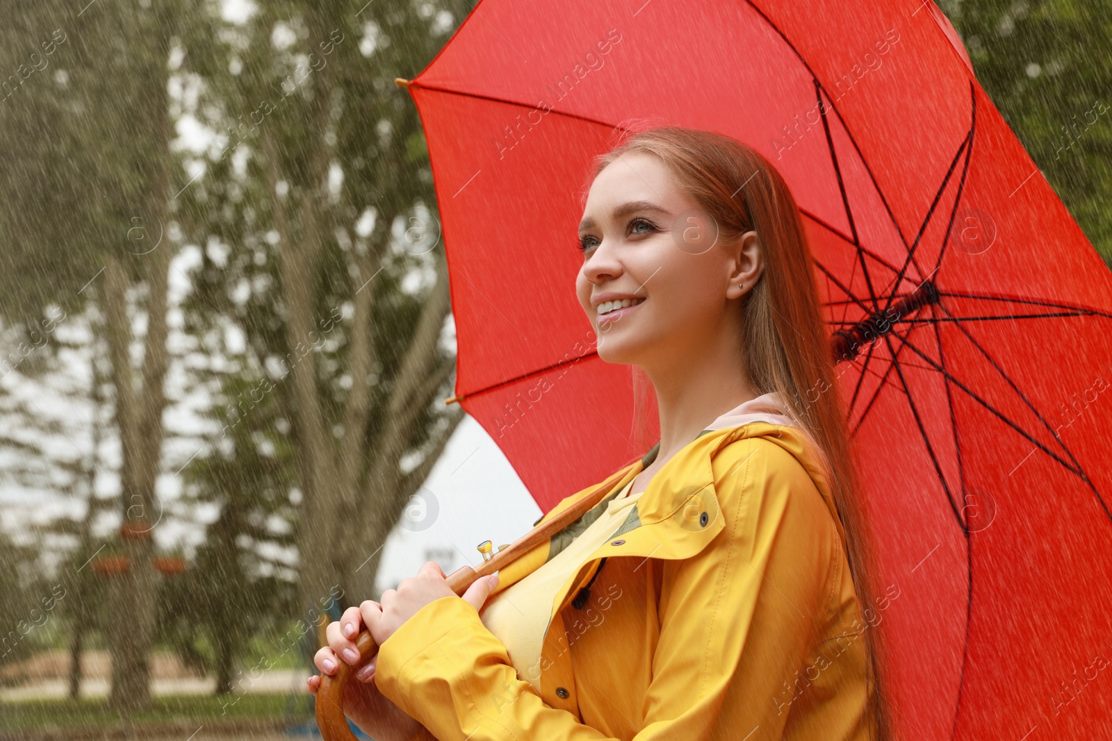 Photo of Young woman with umbrella walking under rain in park