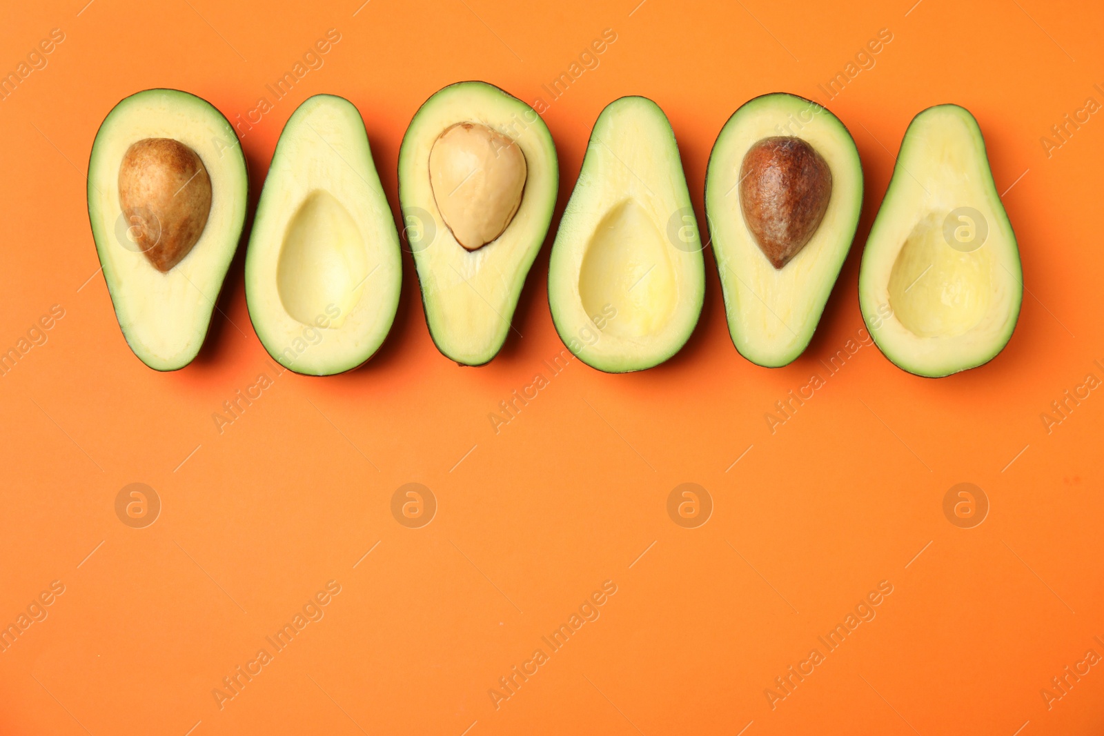 Photo of Cut fresh ripe avocados on orange background, flat lay with space for text