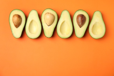 Cut fresh ripe avocados on orange background, flat lay with space for text