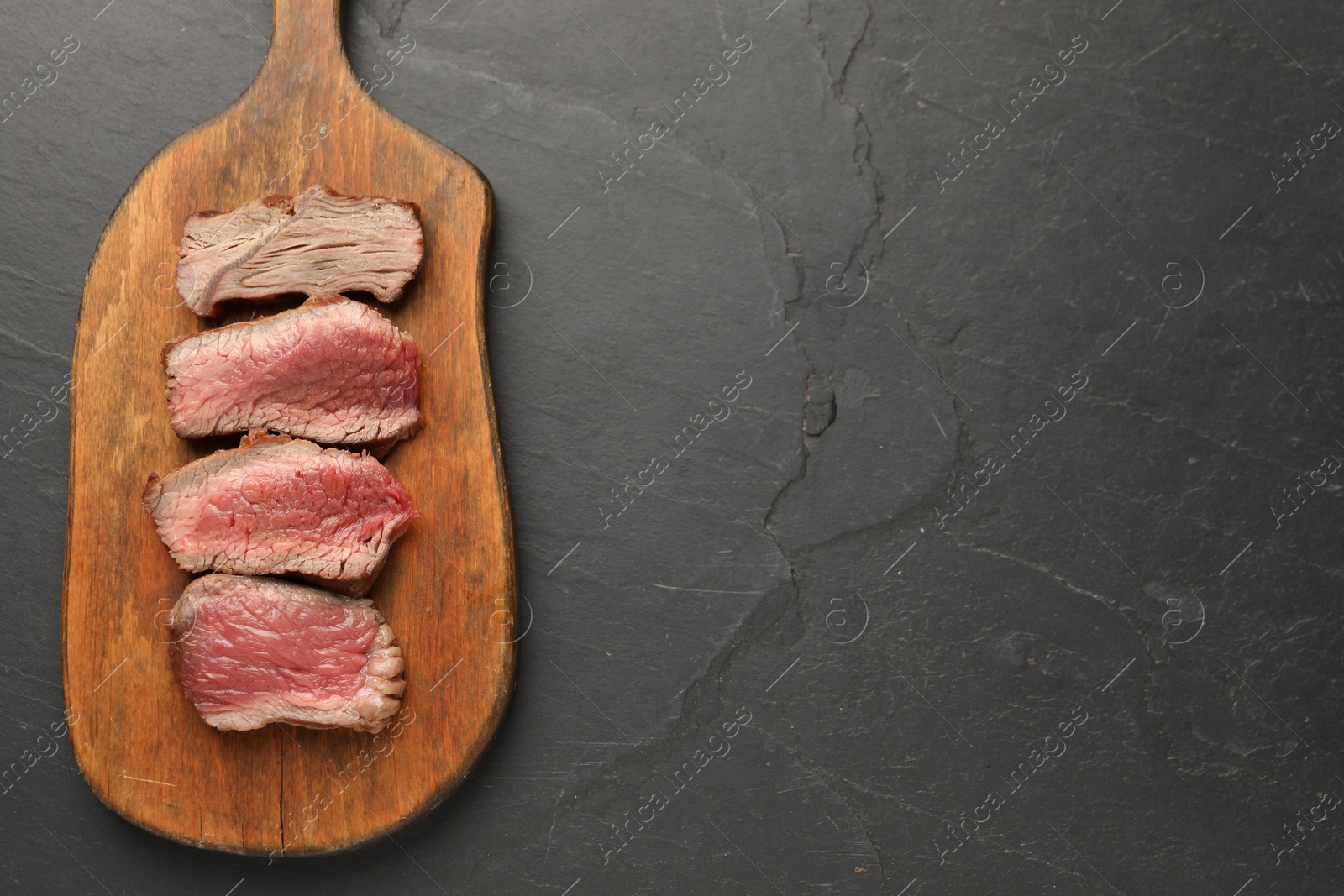 Photo of Delicious sliced beef tenderloin with different degrees of doneness on black table, top view. Space for text