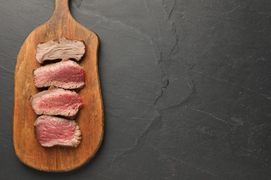 Photo of Delicious sliced beef tenderloin with different degrees of doneness on black table, top view. Space for text